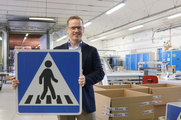 Käsi pitelee pieniä, tummia sylinterimäisiä pellettejä, jotka ovat hajallaan kämmenellä. Taustalla näkyy sininen kangaspäällysteinen pinta ja puinen tuolinjalka