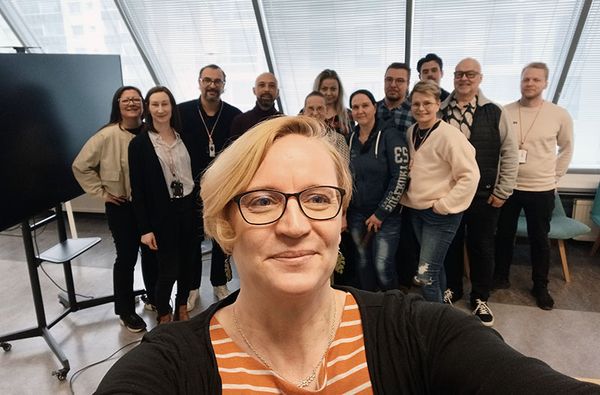 Joukko hymyileviä ihmisiä toimistotilloissa.