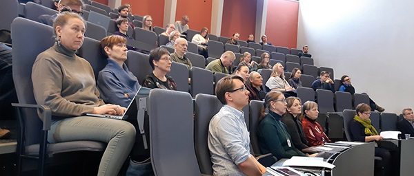 Tapahtuman osallistujia istumassa auditorion penkeillä. 