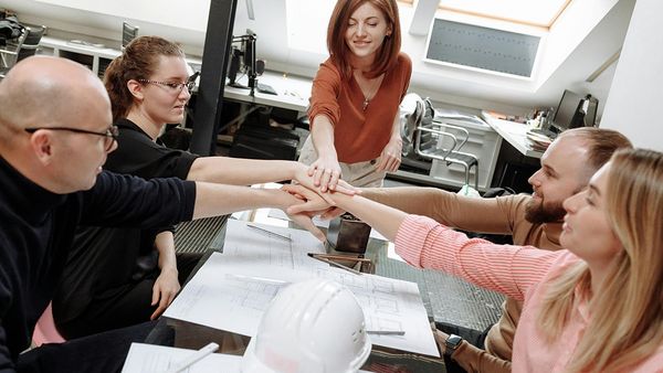 Ihmisiä istumassa pöydän ääressä kädet laitettuina yhteen.