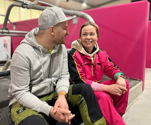 Kaksi ihmistä istumassa vierekkäin navetassa, taustalla vaaleanpunainen seinä. 