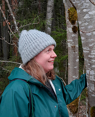 Henkilö seisomassa metsässä puunrungon vieressä.