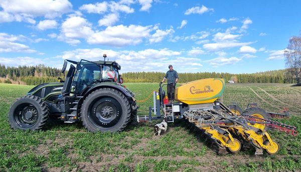 Mies, traktori ja maatalouskone keväisellä pellolla.