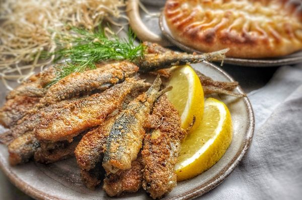 Lautasella paistettuja muikkuja ja sitruunaa, taustalla riisipiirakoita