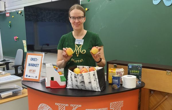 Nainen Martta-paidassa esittelypisteellä koululuokassa.