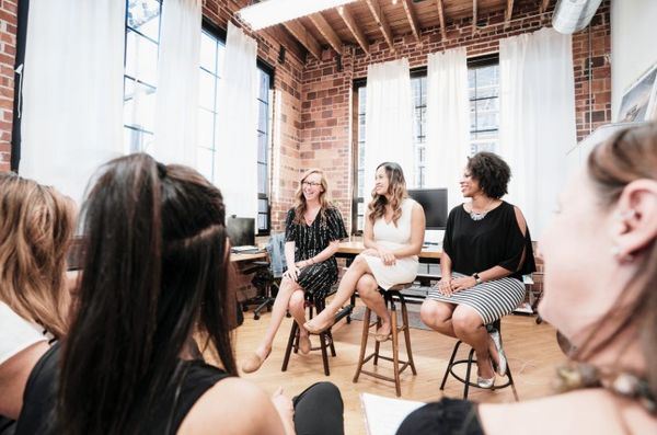 Kuvituskuva. Kolme henkilöä istuu yleisön edessä. Etuosassa kuvaa näkyy yleisössä olevia ihmisiä.