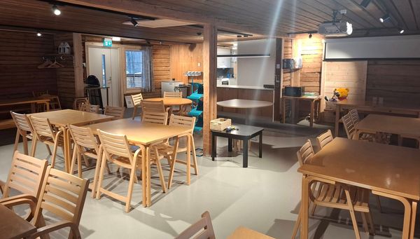 Hirsiseinäinen huone, jossa pöytiä ja tuoleja. 