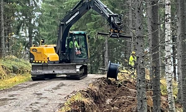 Kaivinkone laskee kaapelia ojaan soratiellä metsässä.