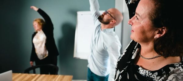 Kuvituskuva: Kuvassa kolme työntekijää tekee taukojumppaa