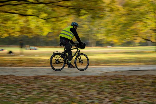 Kuvituskuva: Syksyinen puistomaisema. Mies pyöräilee huomioliivi päällä.