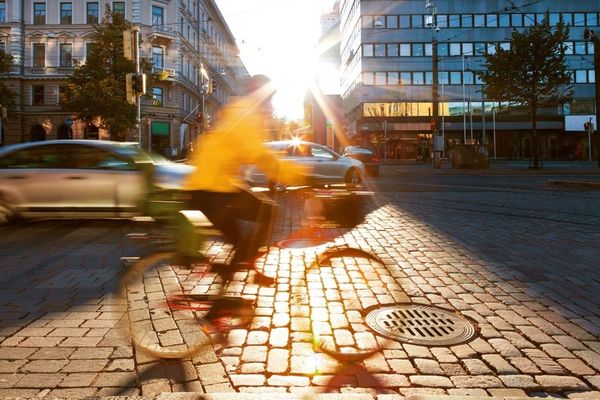 Keltaiseen takkiin pukeutunut pyöräilijä kaupungissa.