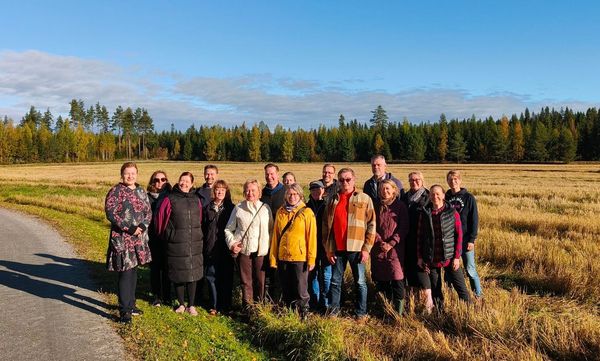 Henkilöitä ryhmäkuvassa pellonreunassa kauniissa syysilmassa.