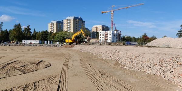 Rakennustyömaalla hiekkakenttä, kaivinkone, kerrostaloja ja nosturi