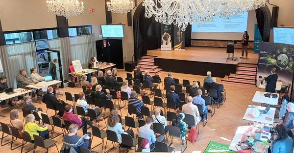 Juhlasali ylhäältäpäin kuvattuna. Ihmisiä istuu ja kuuntelee lavan esitystä