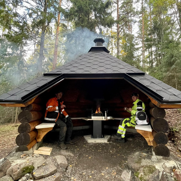 Ihmisiä grillikodassa paistaassa makkaraa