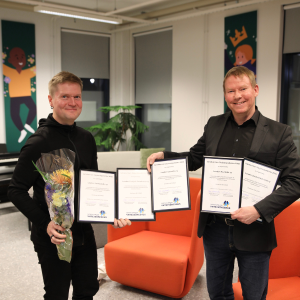 Henkilöt pitävät käsissään viittä palkinoa ja kukkia.