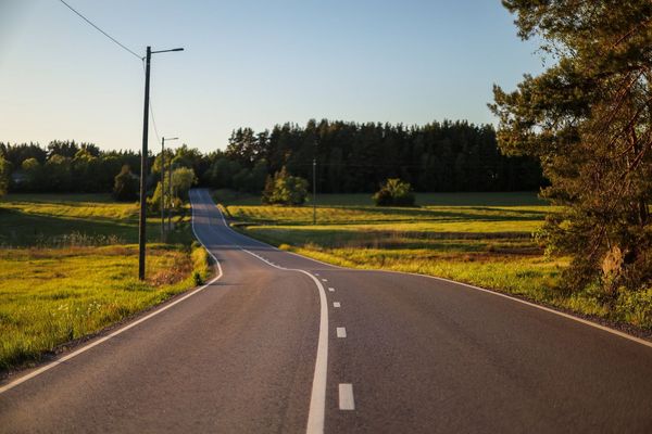Tyhjä maantie, jonka laidalla peltoja ja taustalla metsää.