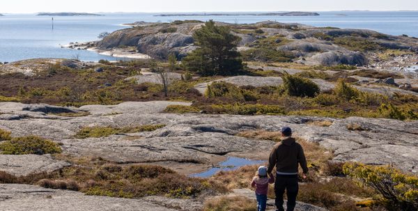 Pieni lapsi aikuisen kanssa kallioisella meren rannalla.