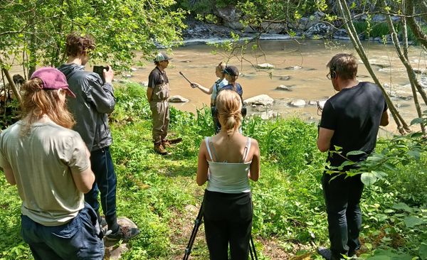Nuoret haastattelevat videolle jokirannassa.
