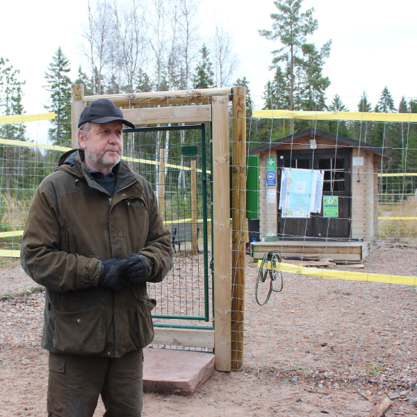 Jakkuvärkin yrittäjä koirametsän portin edessä ulkotakki yllään.