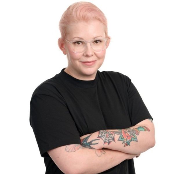 Anu Kantola katsoo suoraan kameraan. Valkoinen tausta.