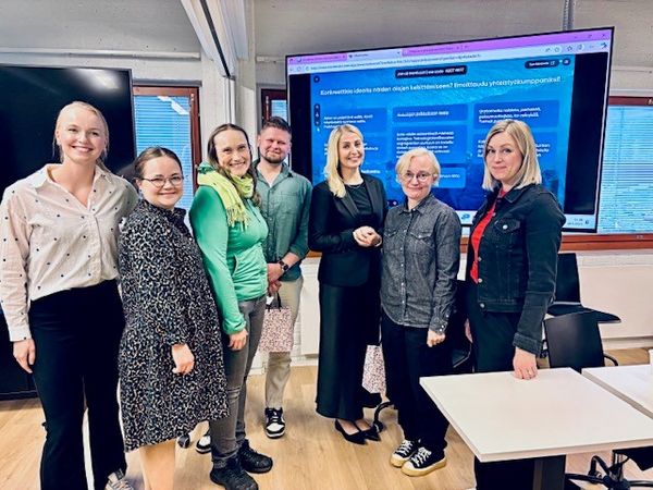 Tilaisuden järjestäjiä ja panelisteja esitysruudun edessä.