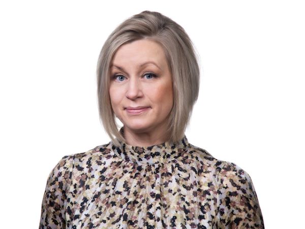 Taina Huusko-Leinonen katsoo kameraan, valkoinen tausta.