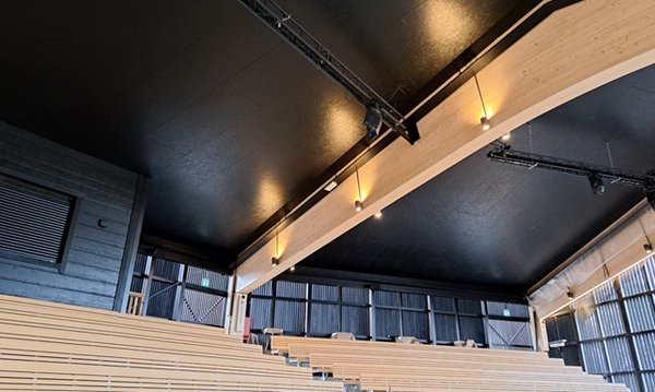 Kuvassa areenan sisätilaa, jossa näkyvät musta katto ja puiste kattopalkit sekä penkkirivit.