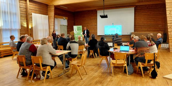 ihmisiä pöytien ääressä kuuntelemassa esitystä.